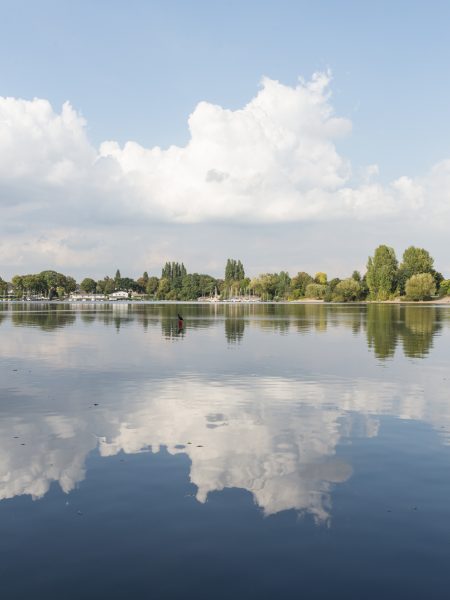 Blick auf einen See indem sich der blaue Himmel und die Wolken spiegeln.