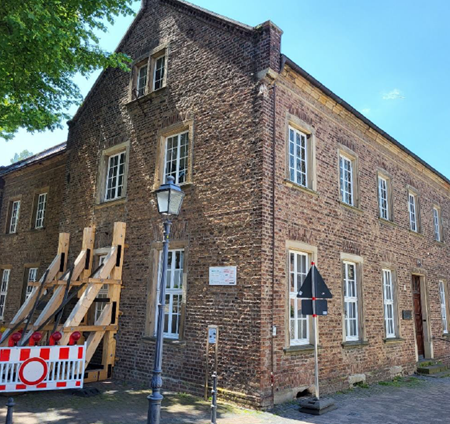 Gebäude "Alte Musikschule" in Merzenich mit Bauzaun und Bakenabstützung am Gebäude links im Bild