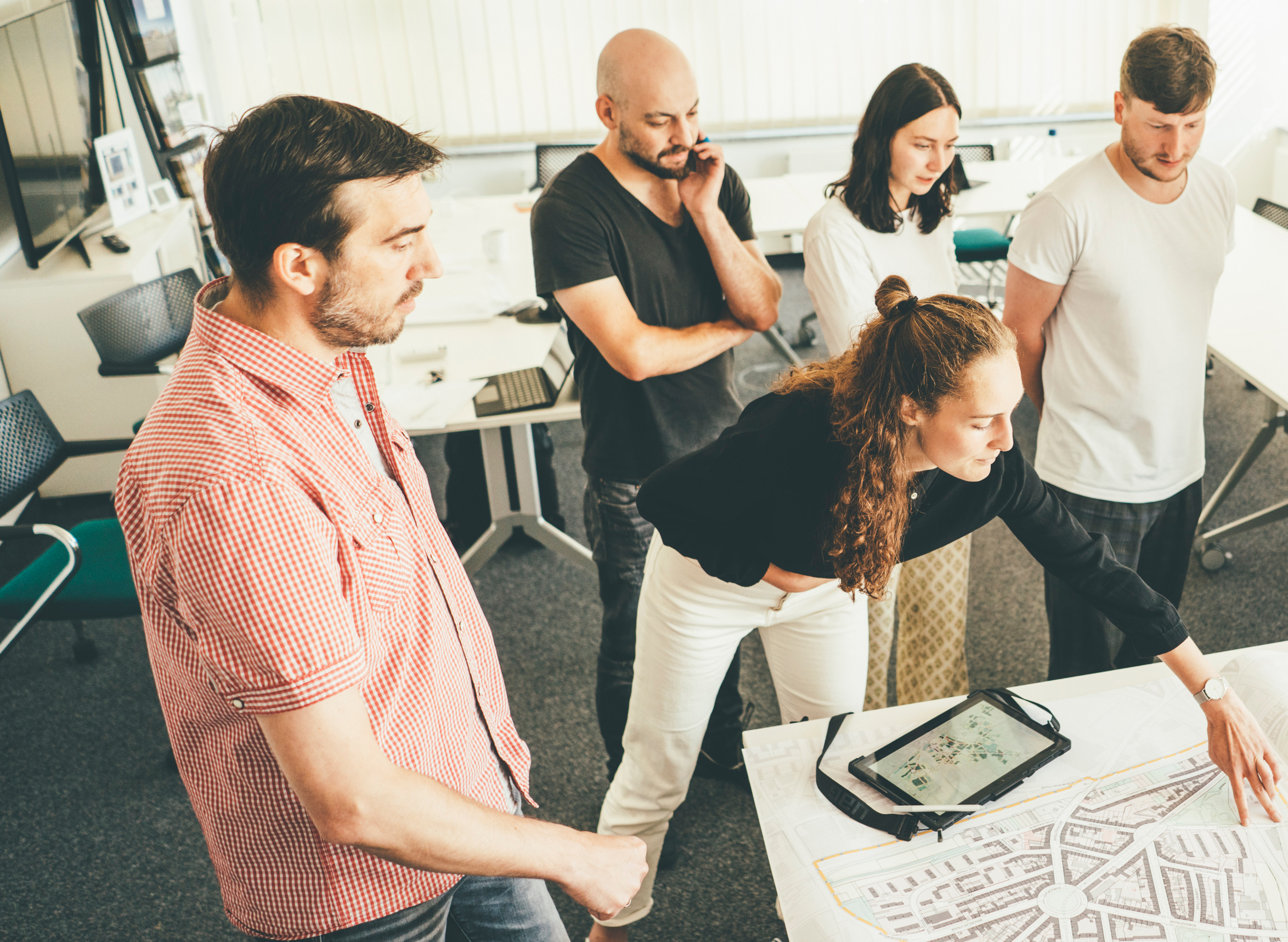 Planungsteam bespricht sich im Büro und zeigt etwas auf einer Karte